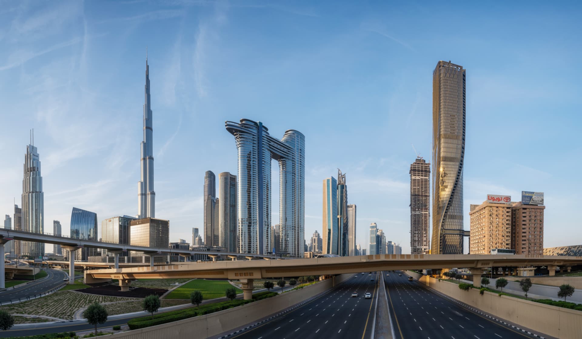 Wide skyline context shot of Wasl Tower with highway and metro line