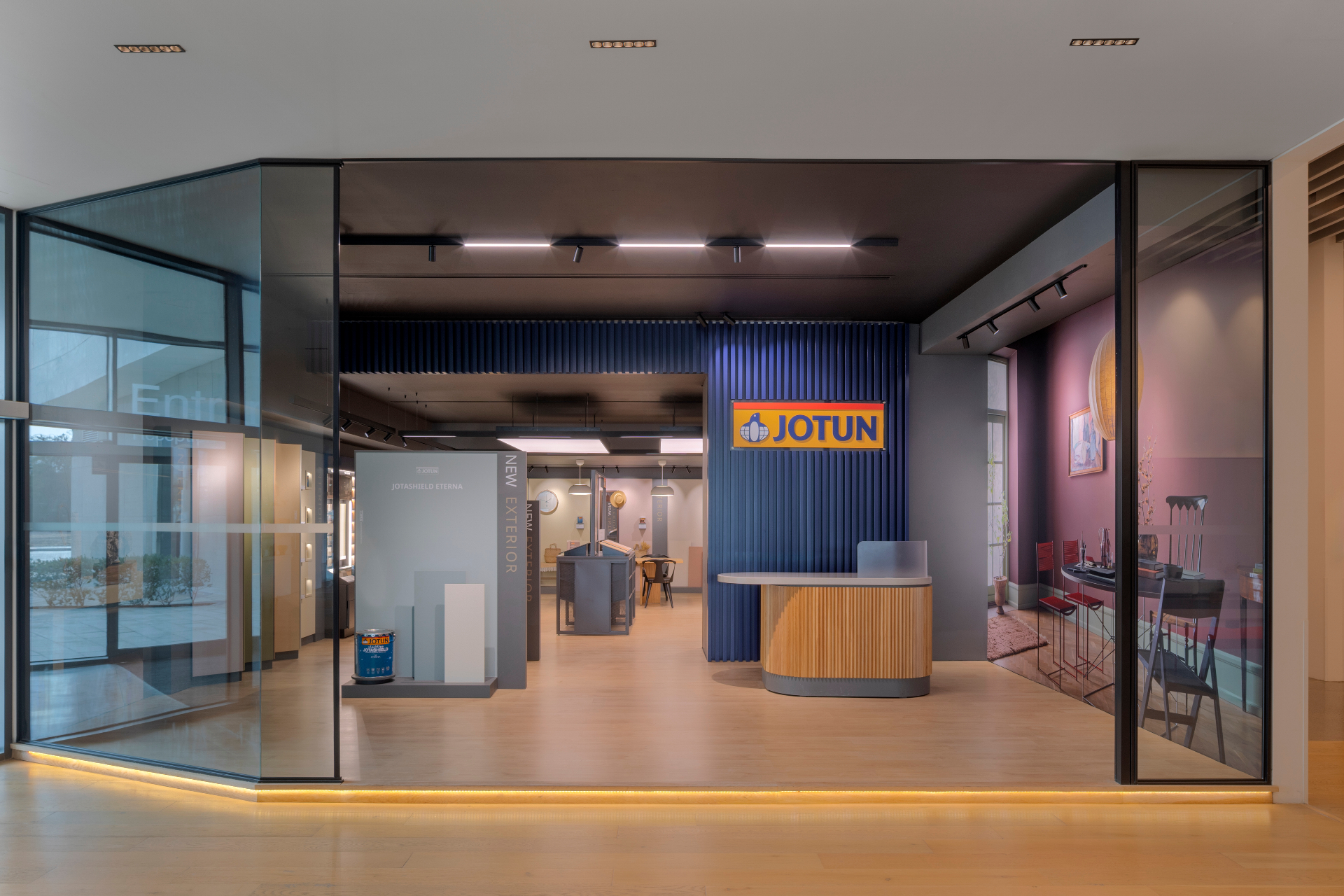 Jotun HQ — interior showroom entrance with the yellow JOTUN sign on a blue slatted wall, reception desk and product displays