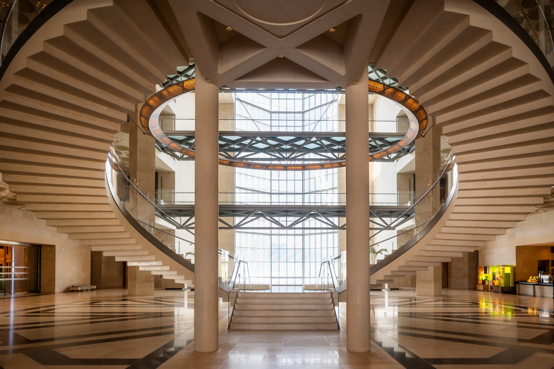 Symmetrical twin curved staircases and suspended ring chandelier in the Museum of Islamic Art atrium, backed by a full-height window wall