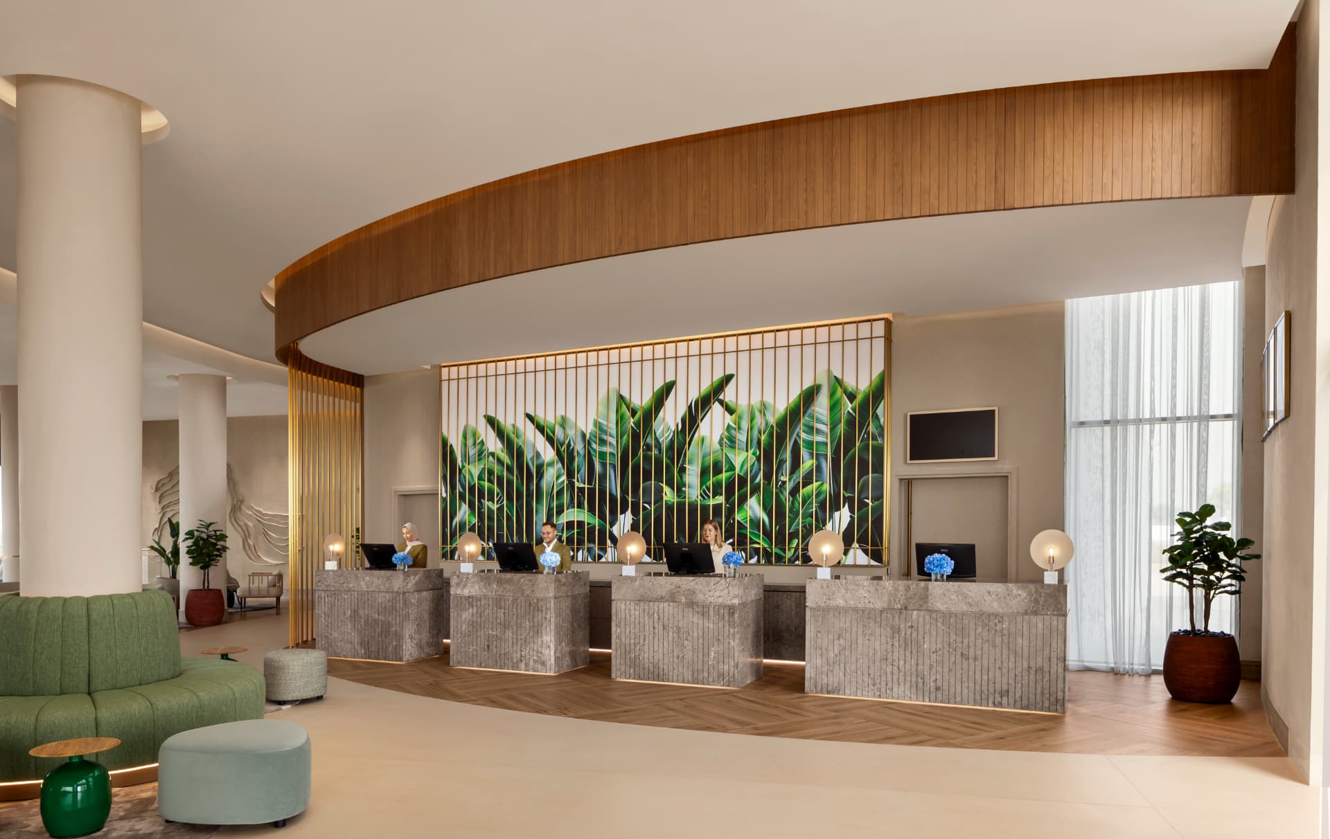 Rotana Ras Al Khaimah reception after the refresh — curved timber soffit, four fluted stone check-in desks lit evenly, and the backlit banana-leaf artwork behind the front-desk team