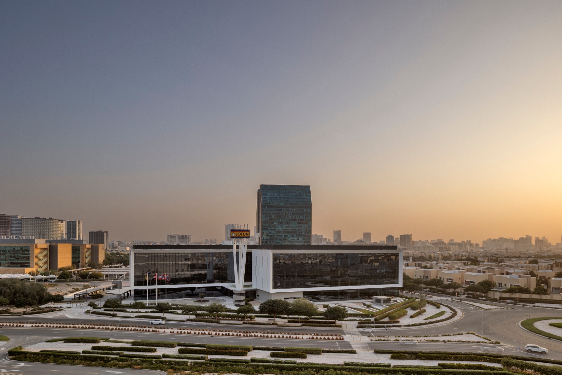 Jotun HQ — elevated dusk composition showing the full HQ building against the Dubai skyline with a warm sunset gradient