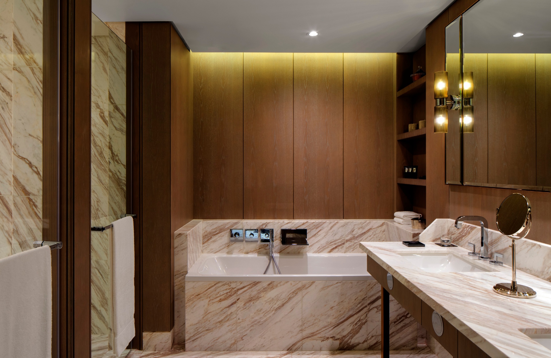 Marble bathroom at The St. Regis with veined stone walls, glass shower and folded towels