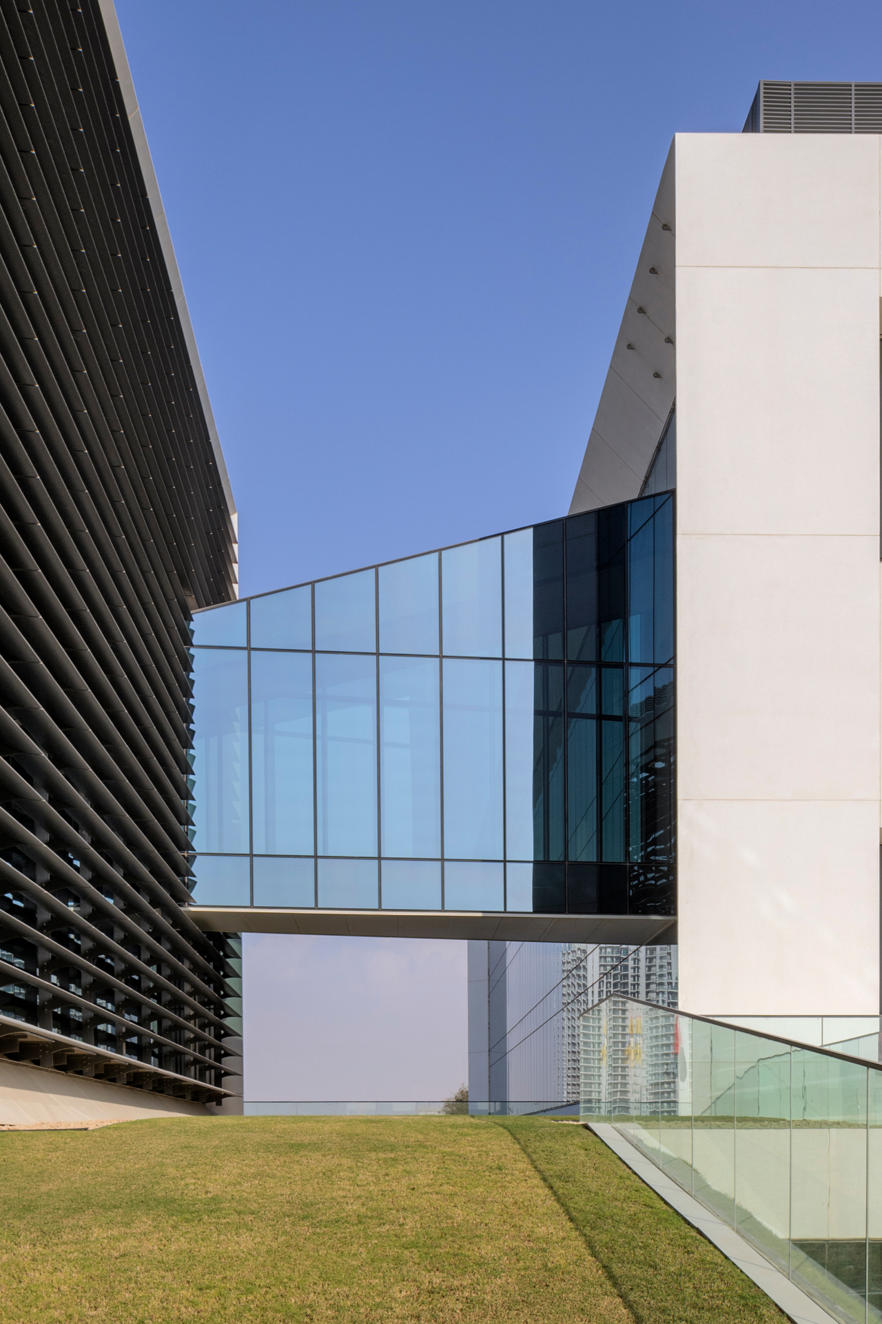 Jotun HQ — vertical view looking up at the glazed bridge structure between the white stone tower and the dark slatted facade against a blue sky